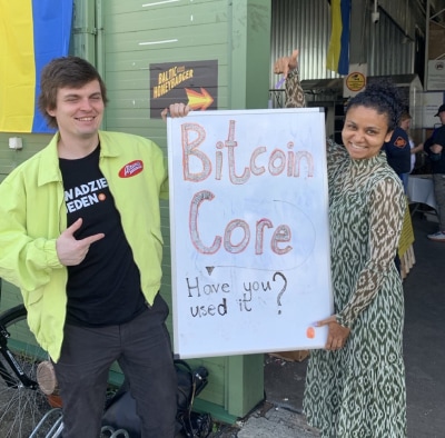 Two contributors holding up a sign that reads 'Bitcoin Core - Have you used it?'